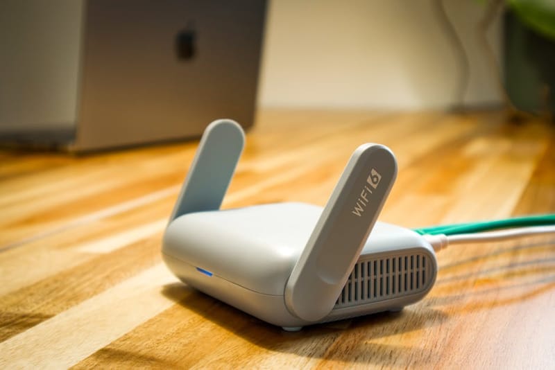 A modern Wi-Fi 6 router with antennas on a wooden desk, representing home networking hardware