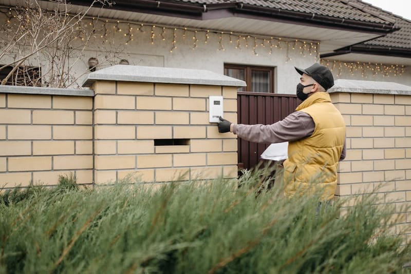Hand pressing a video doorbell button on a home entrance